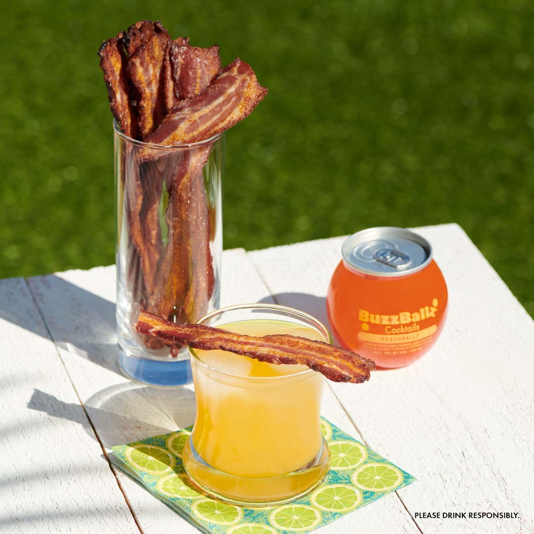 Bacon flavored with BuzzBallz?! 🤯 It’s just as great as you think it would be. 

Ingredients

Cayenne Pepper (optional)
Lemon zest of 2 small lemons
2-4 PeachBallz BuzzBallz
1 lb of thick cut, hickory-smoked or maple-smoked bacon

Instructions
-In a shallow bowl or container of your choice, separate the bacon.
-Pour enough of the PeachBallz BuzzBallz over the bacon to fully submerge it in liquid.
-Cover the bowl in plastic wrap and refrigerate it for 6-8 hours, or overnight.
-Remove the bacon from the liquid and pat it dry with a paper towel.
-Preheat the oven to 400 degrees.
-Place the bacon on a lined baking sheet to avoid sticking.
-Monitor the bacon.
-Baking should take between 10 and 15 minutes, but use judgment to determine when the bacon is done.
-Once the bacon is done and has cooled down a little, skewer the bacon.
-If you desire, sprinkle the bacon with a little lemon zest and cayenne pepper.
-Pour any of our fruity BuzzBallz into a cocktail glass and place a slice of PeachBallz bacon on top of the rim of the glass.